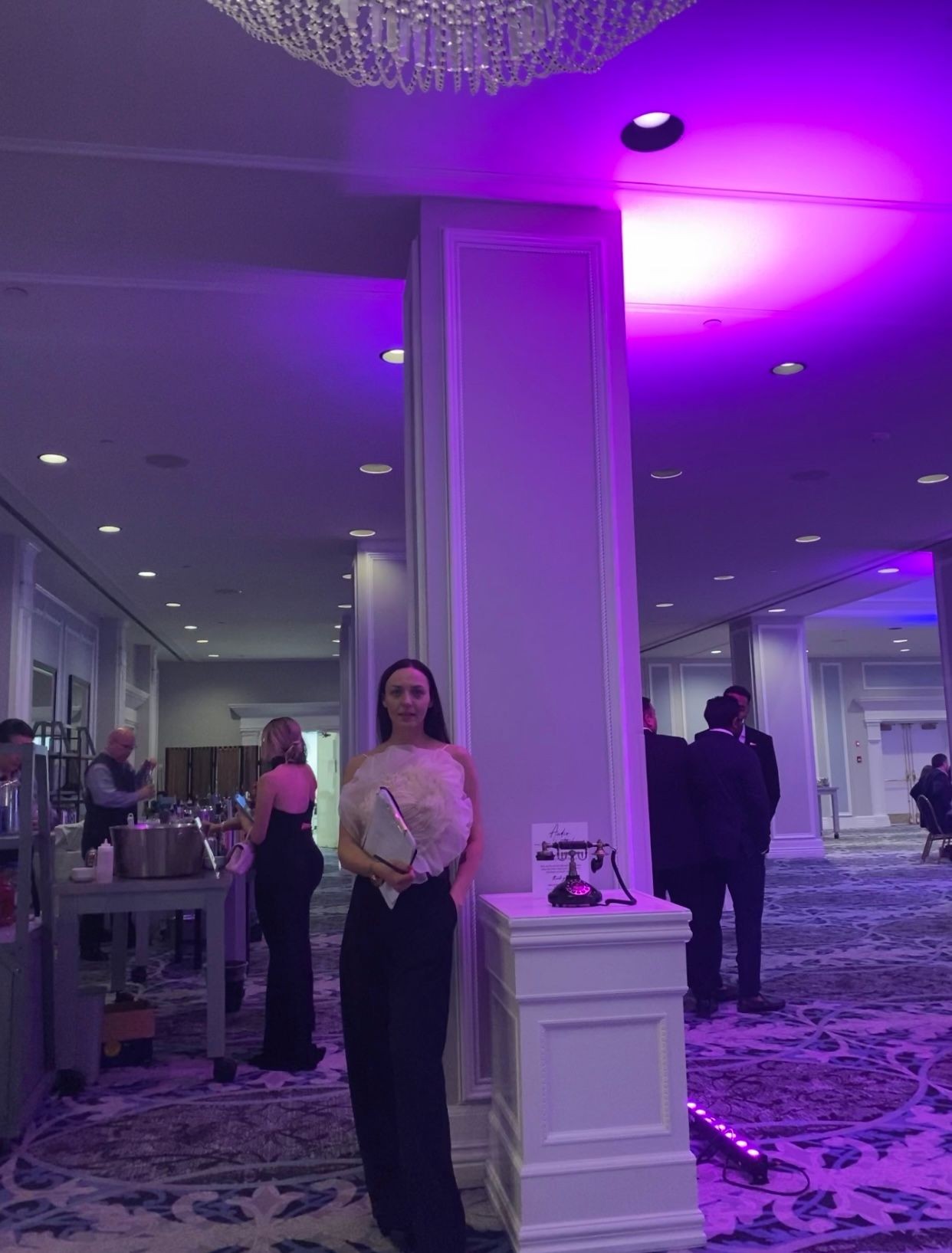 Woman standing in a dimly lit event space with purple lighting and elegant decor.