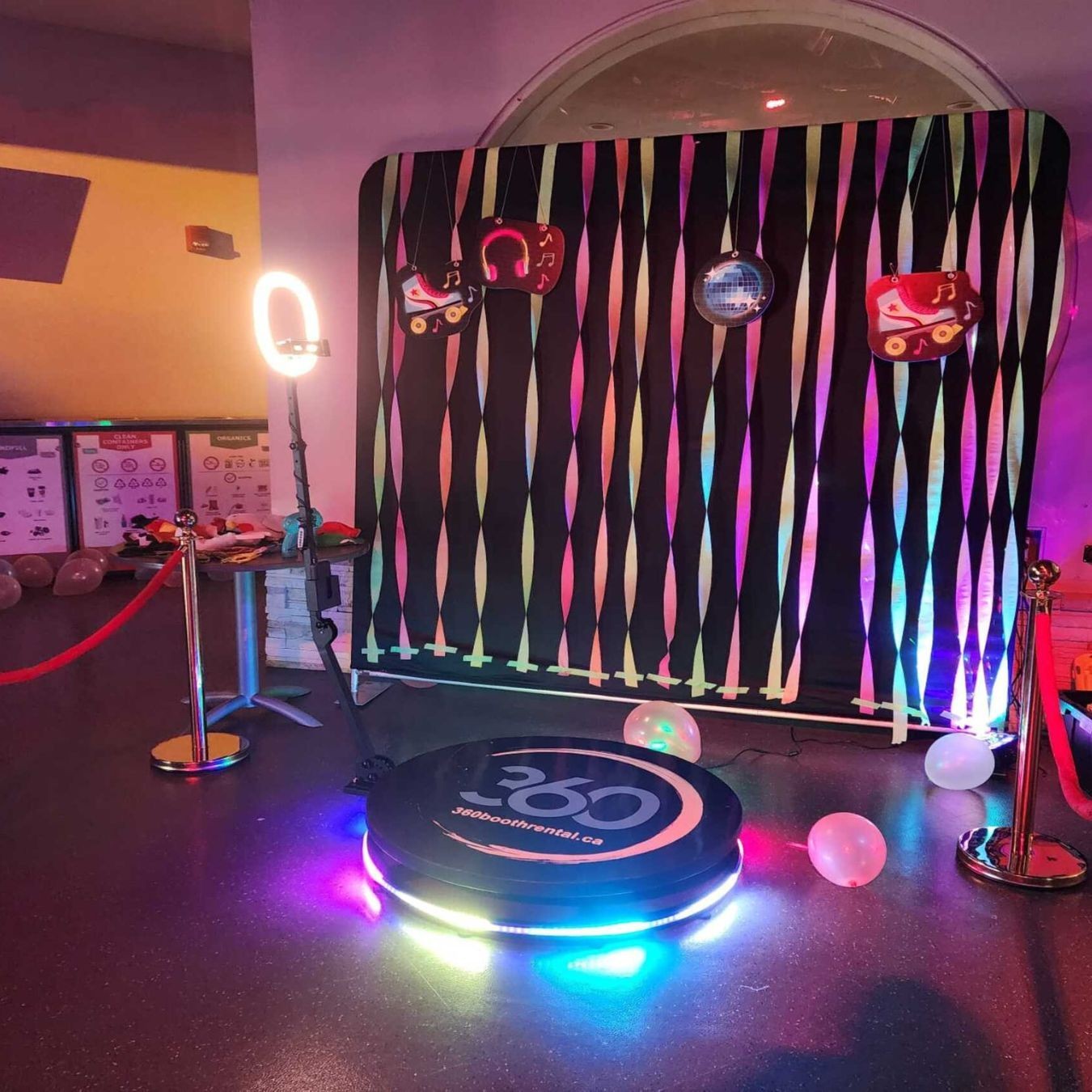 Event setup with a 360 photo booth, colorful backdrop, decorations, and a ring light.